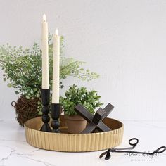 a couple of candles sitting on top of a wooden bowl filled with plants and scissors