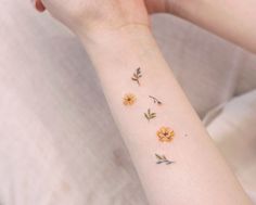 a woman's arm with yellow flowers on the left side of her wrist and two small daisies on the right hand