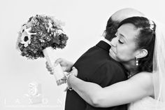 a bride and groom hugging each other in front of a white wall holding a bridal bouquet