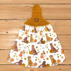 a white dress with dogs and pumpkins is hanging on a wooden wall in front of a wood floor