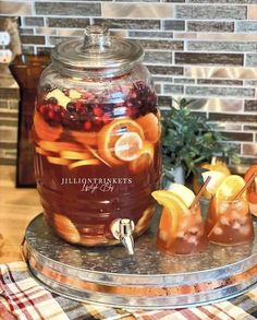 a jar filled with liquid sitting on top of a table next to apples and oranges