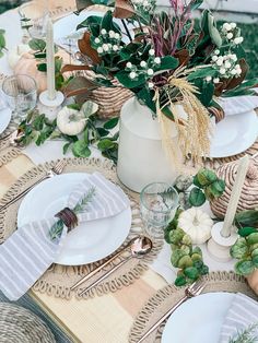 the table is set with white plates, silverware and greenery in vases