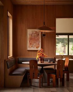 a dining room with wooden paneling and black leather seat covers on the bench, along with a round table surrounded by brown upholves