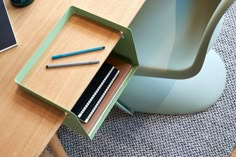 a wooden table topped with a drawer filled with pens and pencils next to a chair