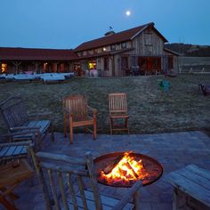 a fire pit with chairs around it in front of a barn at night, lit up by the full moon