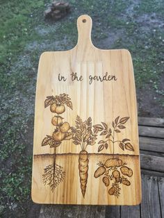 a wooden cutting board with an image of vegetables on it that says in the garden