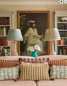 a living room with couches, lamps and pictures on the wall above them in front of bookshelves