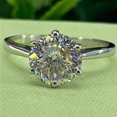 a diamond ring sitting on top of a green table next to a leafy plant