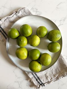 limes are arranged on a white plate next to a towel