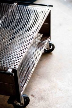 a metal table sitting on top of a floor next to a black drawer with wheels