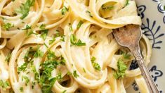 a plate full of pasta with parsley on top and a spoon in the bowl