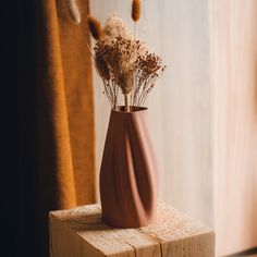 a vase with dried flowers in it sitting on a wooden block