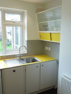 a small kitchen with yellow counter tops and white cupboards next to a large window