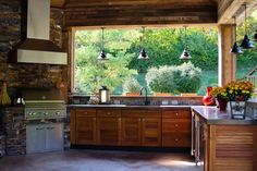 an outdoor kitchen with wood cabinets and stainless steel appliances is shown in the foreground