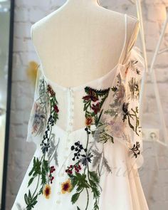 a white dress with flowers and leaves on the front, sitting on a mannequin