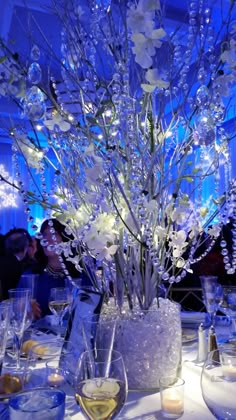 a vase filled with lots of white flowers on top of a table covered in wine glasses