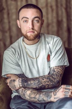 a man with tattoos on his arms and chest sitting in a chair looking at the camera