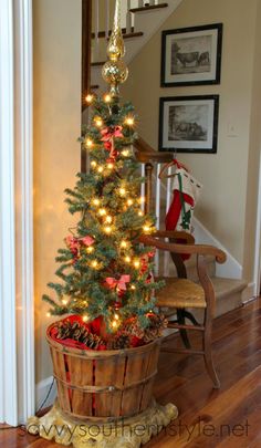 a small christmas tree in a wooden bucket on the floor next to a stair case