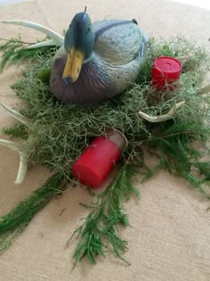 a duck sitting on top of a pile of moss next to two red candle holders