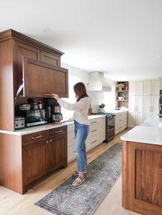 a woman standing in the middle of a kitchen reaching for something on the counter top