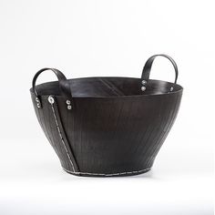 a black leather basket with white stitching on the sides and handles, sitting in front of a white background