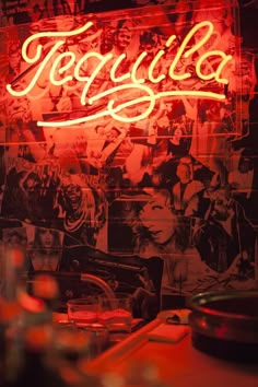 a neon sign that says tequila with pictures of people on the wall in the background