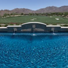 a large swimming pool in the middle of a golf course with mountains in the background