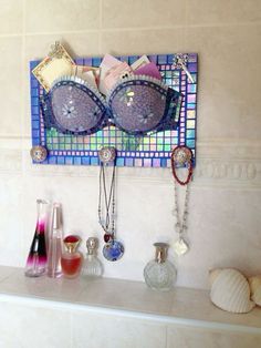 there is a mirror and jewelry on the shelf in this bathroom that has been decorated with mosaic tiles