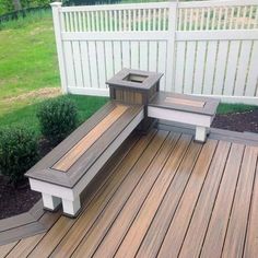 a wooden deck with two benches and a trash can on the back side, in front of a white picket fence