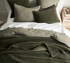 a bed covered in green and white linens next to a night stand with two nightstands