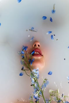 a woman is floating in the water with blue flowers around her and she has her eyes closed