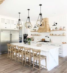 a kitchen with white cabinets and wooden floors has an island in the middle that is surrounded by chairs