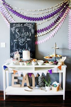 a white table topped with cake next to a chalkboard and bunting streamers