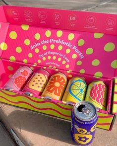 an open pink box with six cans of soda on the ground next to each other