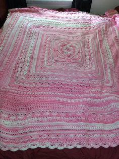 a pink crocheted blanket sitting on top of a bed next to a window