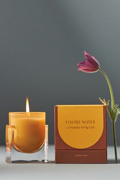 a candle with a flower in it next to a box and a single pink flower