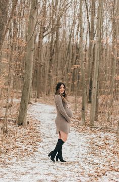 a pregnant woman standing in the middle of a snowy forest with her hands on her hips