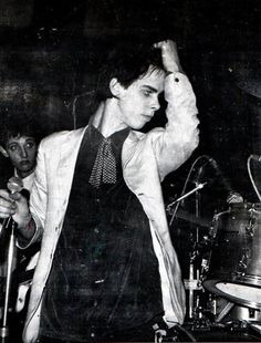 a man in a suit and tie holding his hand up to his head while standing next to a drum set