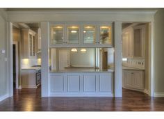 an empty kitchen with wooden floors and white cabinets in the center, is seen from across the room