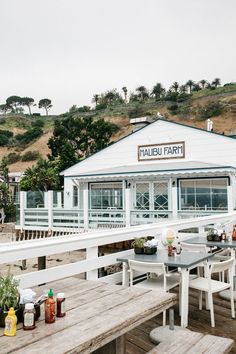 an outdoor dining area with wooden tables and benches on the side of a hill next to a white building