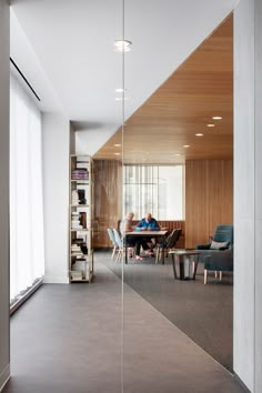 a glass wall in the middle of a room with people sitting at a table and bookshelves