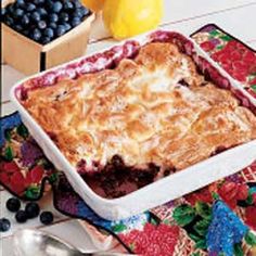 a blueberry cobbler is shown on a colorful placemat with berries and lemons in the background