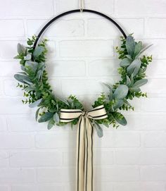 a wreath with green leaves and ribbons hanging on a brick wall