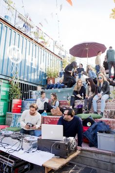 a group of people sitting on top of a pile of luggage with umbrellas over their heads