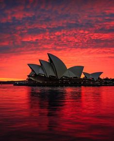 the sydney opera house is lit up in red and blue at sunset, as seen from across the water