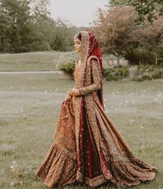 a woman in a red and gold wedding dress is standing in the middle of a field