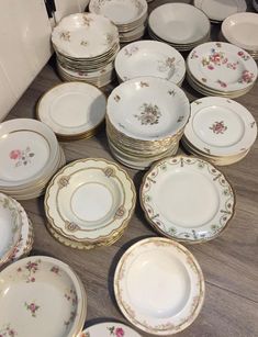 a table topped with lots of white and gold plates on top of a wooden floor