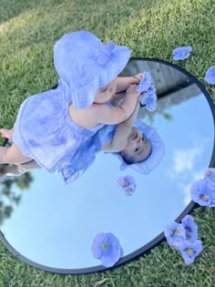 a baby in a blue dress is looking at herself in a mirror with flowers on it