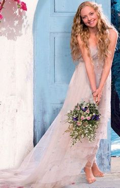 a woman standing in front of a blue door wearing a white dress and holding a bouquet