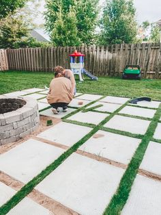 a person kneeling down on the ground in front of a fire pit with grass covering it